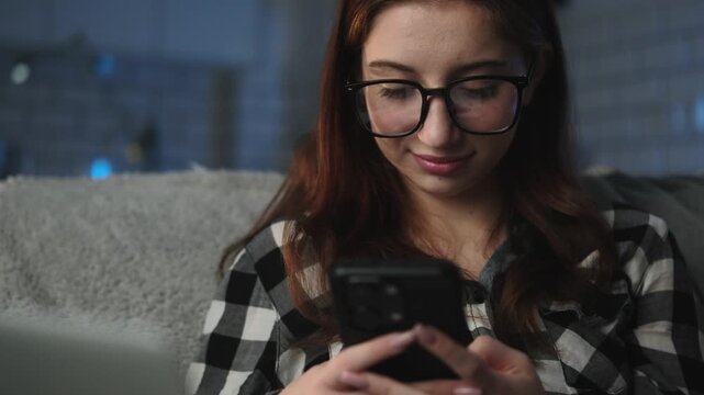 Young Attractive Girl Types A Message To Friend On Smartphone At Home During The Night