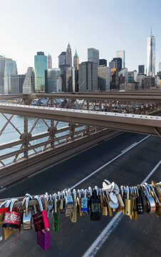 Love locks attached to a metal railing over the East River with the downtown skyscraper skyline, symbolizing romance and urban tourism at the Brooklyn Bridge, Lower Manhattan, New York City.