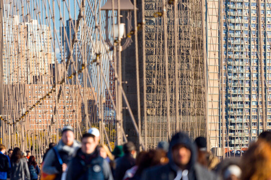 Pedestrians walking across the Brooklyn Bridge with iconic steel suspension cables and Manhattan skyline, representing urban travel, tourism, and lifestyle in New York City, USA.