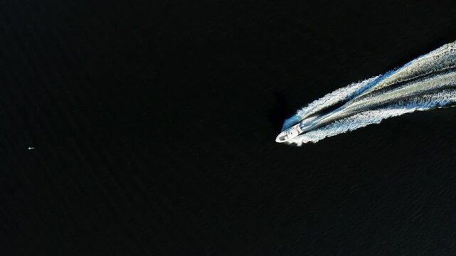 Small speedboat sweeps a sharp curve, carving bright twin wake trails against a wide field of dark water.