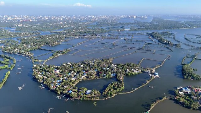 Drone shot capturing the panoramic wetlands of Kadamakkudy with expansive backwaters, fish farming enclosures, narrow causeways, and lush green islets creating striking geometric patterns from above.