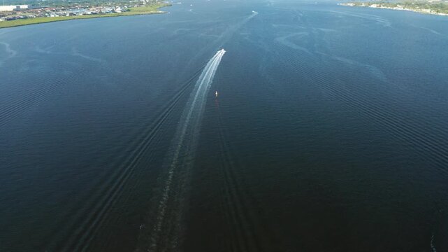 Single motorboat speeds away from the camera, carving a long wake toward the distant Manatee River shoreline under clear daylight.
