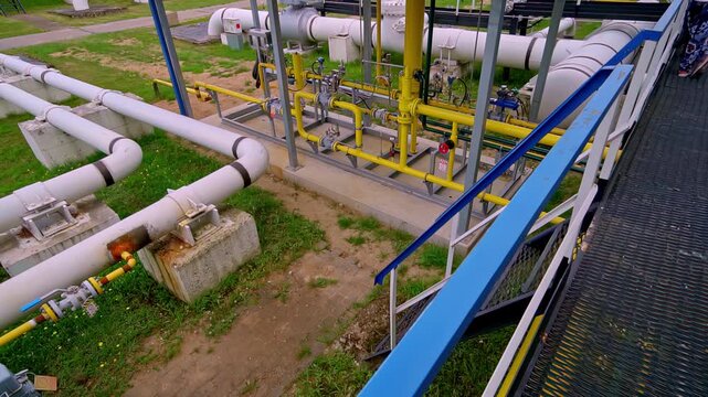 Elevated view of outdoor gas pumping station with large white pipelines on concrete supports yellow gas pipework valves regulators and instrumentation across green grass
