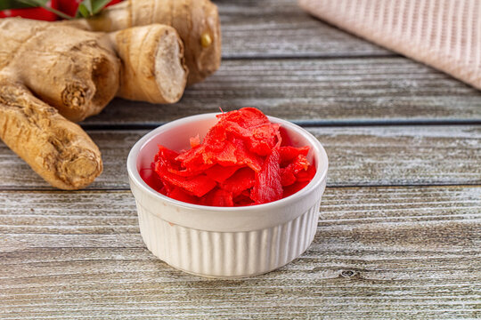 Red pickled ginger in white bowl with fresh horseradish roots on wooden table