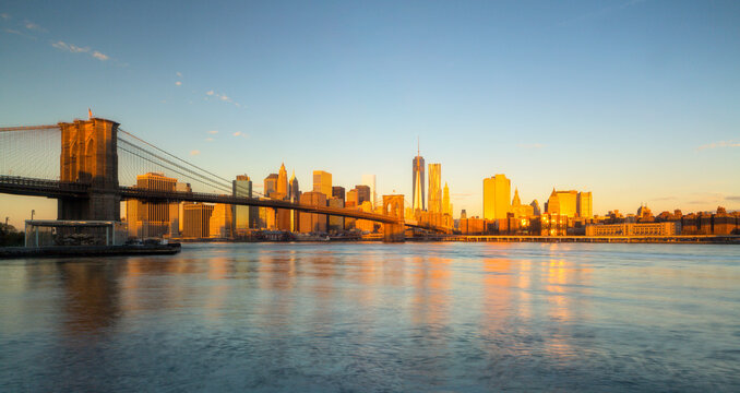 Brooklyn Bridge and Manhattan skyline glow at golden hour above the East River, showcasing urban tourism and travel exploration in Brooklyn Bridge, Lower Manhattan, New York City, USA.
