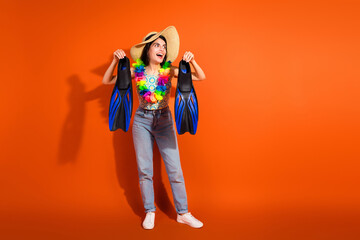 Happy young woman holding swim fins against vibrant orange background, celebrating vacation and summer adventures in a casual style © deagreez
