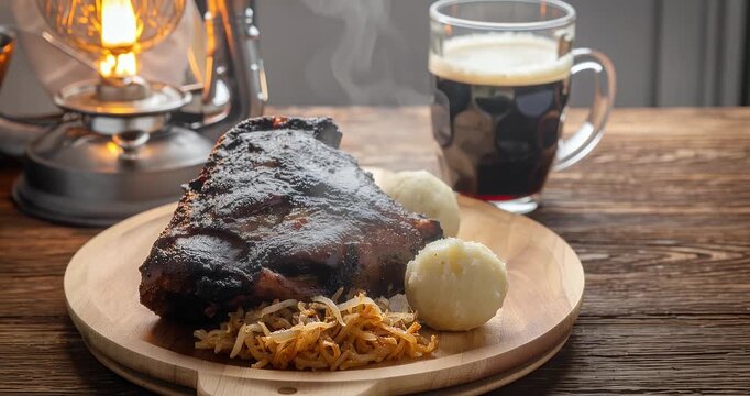 A traditional German meal featuring a roasted pork knuckle with potato dumplings and sauerkraut, served alongside a dark beer and illuminated by a vintage lantern.