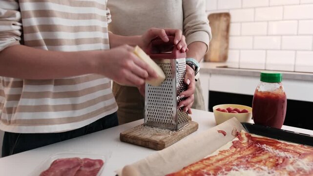 Mom And Daughter In The Kitchen Cooking Homemade Pizza, Shredding Parmesan Cheese