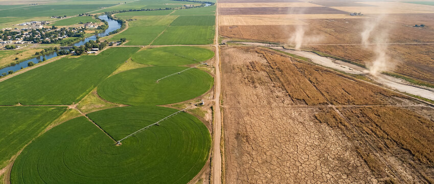 Aerial view contrasting irrigated green agriculture fields with dry, cracked drought land and dust devils