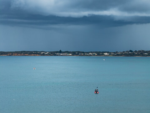 Aerial view of a tiny boat on a calm bay under rain falling from a dark stormy sky