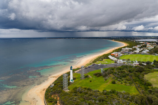 Aerial view of dramatic cloud bank and rain advancing over a coastal lighthouse above a beach