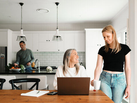 Daughter serving tea to her mother working with her laptop while her father checks the vegetables