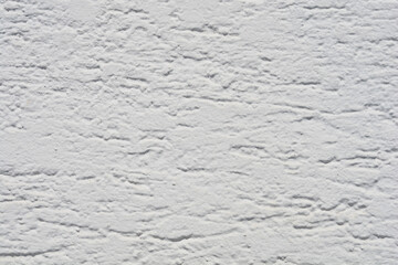 Fototapeta premium A close up full frame view of a white painted exterior wall surface featuring a rough decorative stucco plaster texture with horizontal grooves