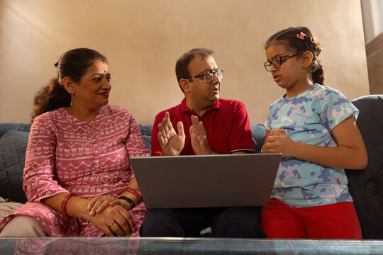 Parents guiding their daughter with a laptop in the living room