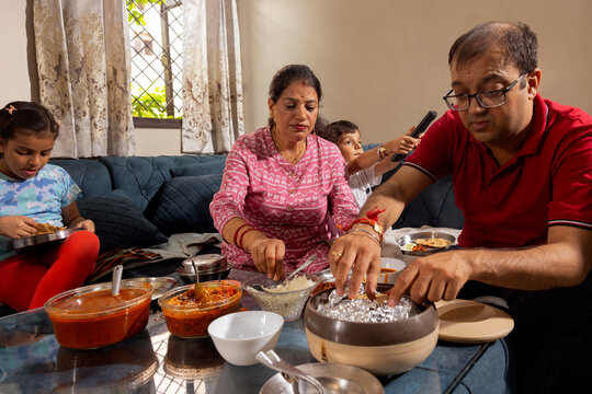 wife serving food to her husband while daughter is eating and son is turning on the tv in background