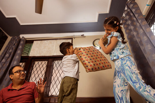 pillow fight between siblings and father watching in background