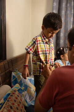 father helping his son in buttoning up his shirt and daughter in background