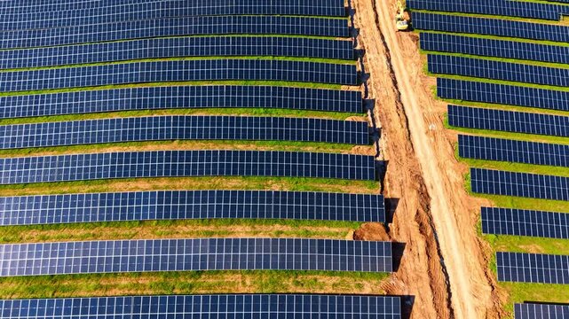 Top down view of parallel solar panel rows on grass. High angle geometric pattern of photovoltaic solar panels installed on green field with dirt track.