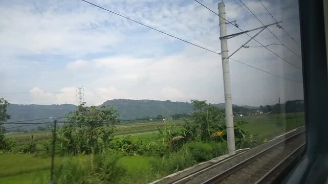 Train POV Passing Green Rice Paddies and Hills with Railway Catenary in Rural Java Indonesia