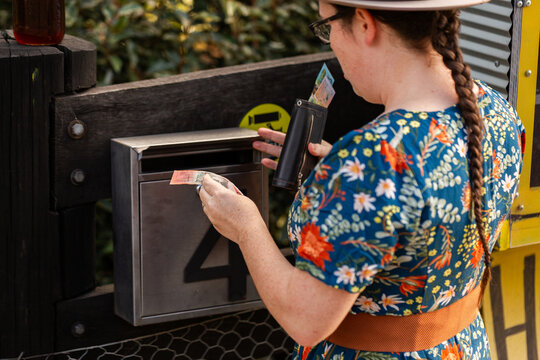 woman paying for produce at roadside stall using honesty box system putting cash in mailbox