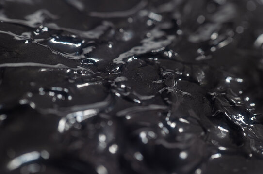 Close view of a black liquid with shiny surface in a stark setting
