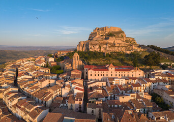 Obraz premium Aerial view of Morella medieval town at sunrise, showing terracotta rooftops, Gothic church tower, convent building and hilltop castle, Els Ports, Castellon, Spain