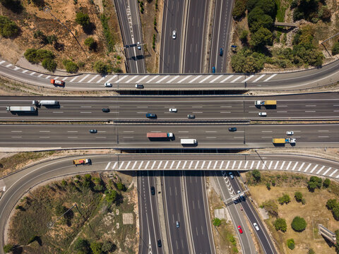 Top-down aerial view of a multilane motorway interchange overpass in Spain with live traffic including trucks and cars, illustrating transport infrastructure and road freight logistics