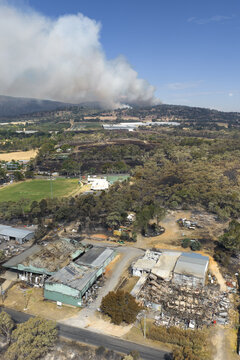 Aerial view of a large bushfire burning on a distant hillside behind destroyed factory shed