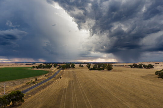 Aerial view of rain falling from dramatic storm clouds over dry paddocks