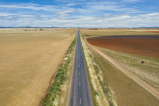 Aerial view of long straight country road through farmland under a sky full of lenticular clouds