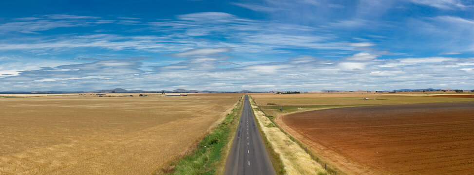 Aerial panorama view of straight country road through farmland under a sky full of lenticular clouds