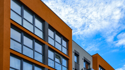 Obraz premium Modern residential building facade against blue sky. Contemporary apartment house architecture with orange walls and windows.