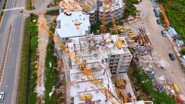 Aerial view of yellow tower crane boom over construction site. High angle view of a yellow crane arm over an uncompleted concrete building floor next to an asphalt highway.