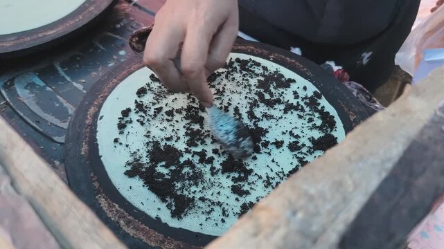 A hand is spreading a dark topping evenly over a batter. 