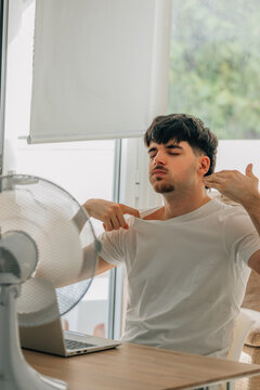 young man at home studying and working on a laptop during a summer heat wave