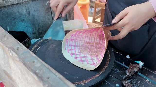 Hands are lifting a crispy, thin crepe from a hot griddle.