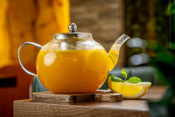 Sea buckthorn citrus tea in glass teapot on board. Hot orange sea buckthorn tea in transparent glass teapot next to a lemon slice and mint leaf on wooden board. © Анна Терелюк
