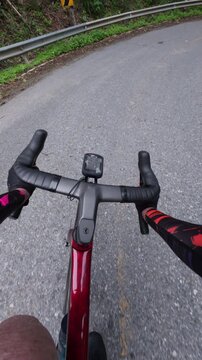 A cyclist's view from the handlebars on a winding mountain road, surrounded by greenery and safety railings.