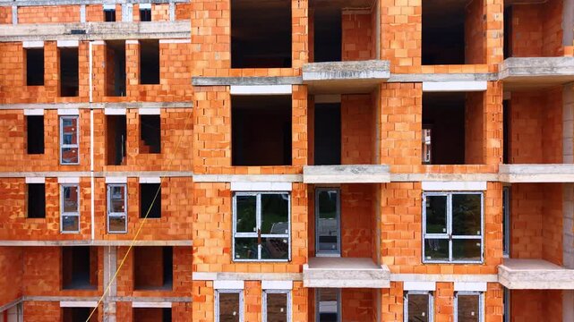 Close up view of residential building brick wall facade. Front view of unfinished multi story house facade made of orange clay blocks with installed windows.