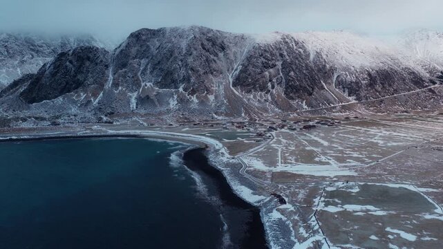 Aerial backdrop of snowy Arctic coastline curving beside calm blue sea, drone establishing background, orbit clockwise