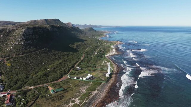 Forward push aerial drone shot toward Slangkop Lighthouse along rugged Atlantic coastline Kommetjie Western Cape South Africa clear daylight