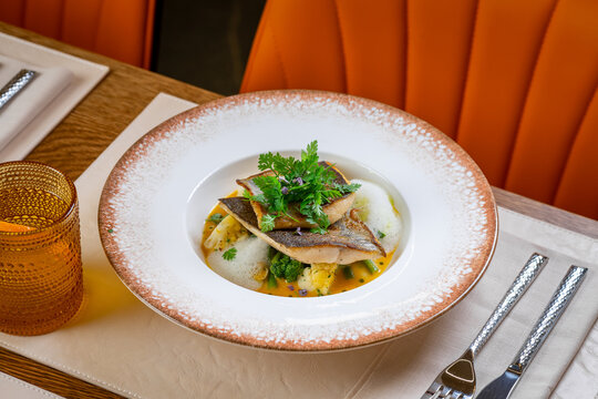 Tasty meal in a restaurant. A plate of fish is garnished with herbs and served with a side. The setting shows a dining table in a restaurant.