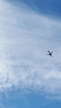 Plane crossing blue cloudy sky on sunny day filmed with phone camera vertical ugc style video. Point of view from ground looking above and up to sky as airplane flying across frame. Vacation holiday