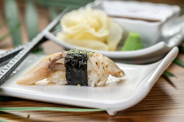 Cured mackerel nigiri sushi with nori seaweed band. Side view of seared mackerel nigiri wrapped in nori seaweed on white plate with blurred background. © Анна Терелюк