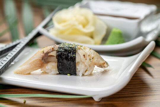 Cured mackerel nigiri sushi with nori seaweed band. Side view of seared mackerel nigiri wrapped in nori seaweed on white plate with blurred background.