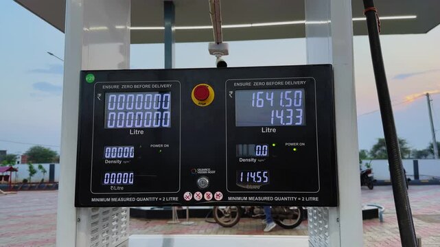 Wide shot of an Indian fuel station dispenser showing a running meter as petrol is being filled into a vehicle, displaying real time fuel volume and transaction value.