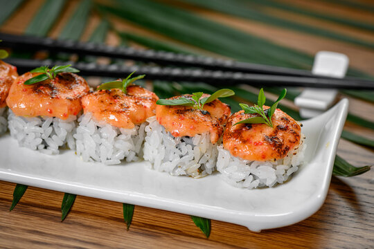 Fresh sushi rolls served with chopsticks. A plate holds sushi rolls made with rice and seafood, garnished with green herbs, ready to eat with chopsticks.