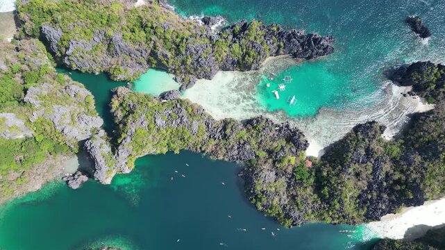 Top-down aerial of Small and Big Lagoon in El Nido, Palawan, featuring tour boats, kayakers and swimmers in coral shallows and turquoise water coves hidden among tropical limestone landscape