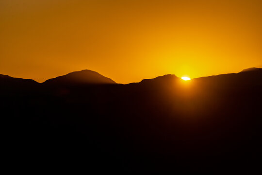 View of the sun setting behind the silhouetted mountain peaks under a vibrant orange sky in Maseru, Maseru, Lesotho.