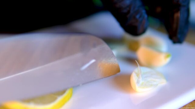 Chef in black gloves slicing fresh garlic beside lemon slices on white porcelain board during food preparation